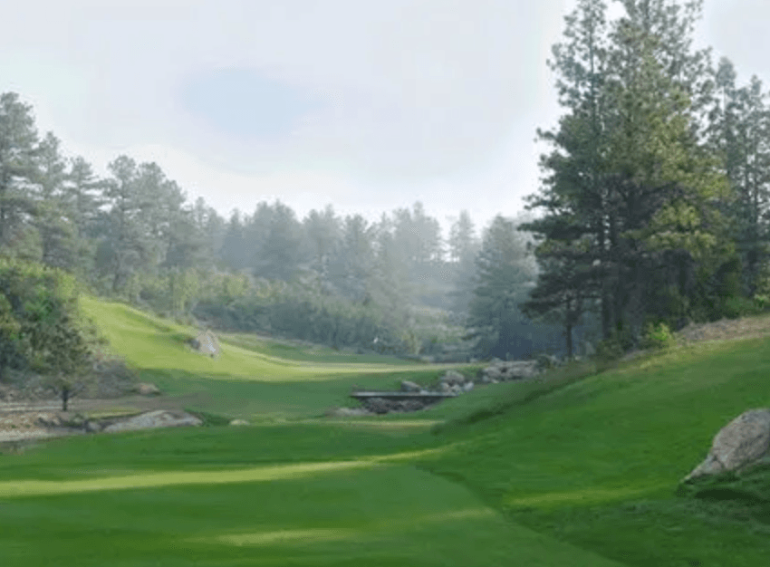 View of Hole 17 at The Golf Club at Bear Dance, framed by pine trees and rocks.